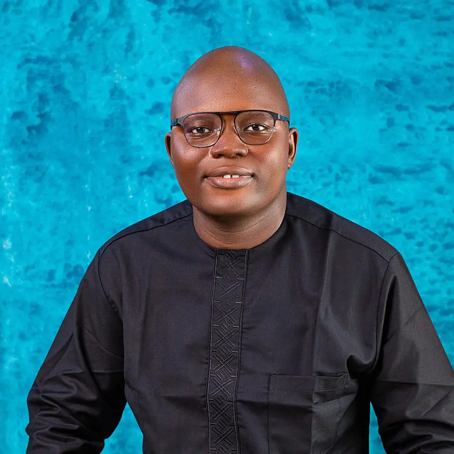 Headshot of a smiling Sierra Leonian man wearing a black shirt and glasses