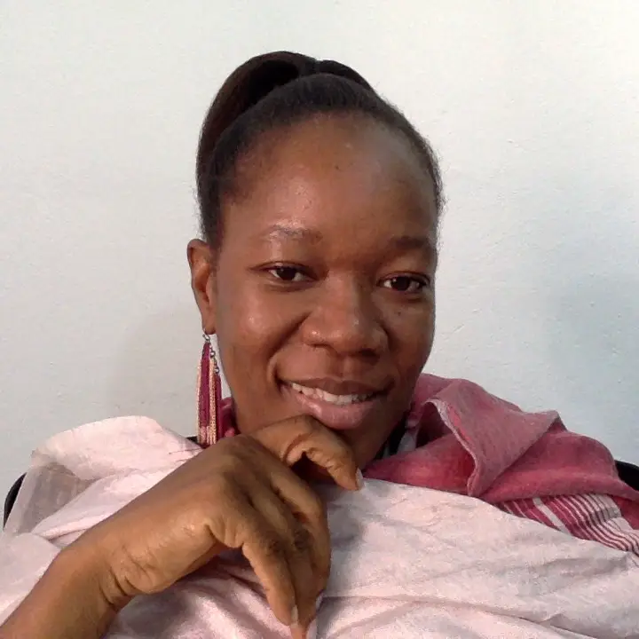 Headshot of a smiling Sierra Leonian woman with scraped back hair and a pink scarf and top
