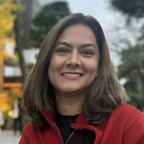 Headshot of a smiling Nepali woman with long brown hair and a red jacket