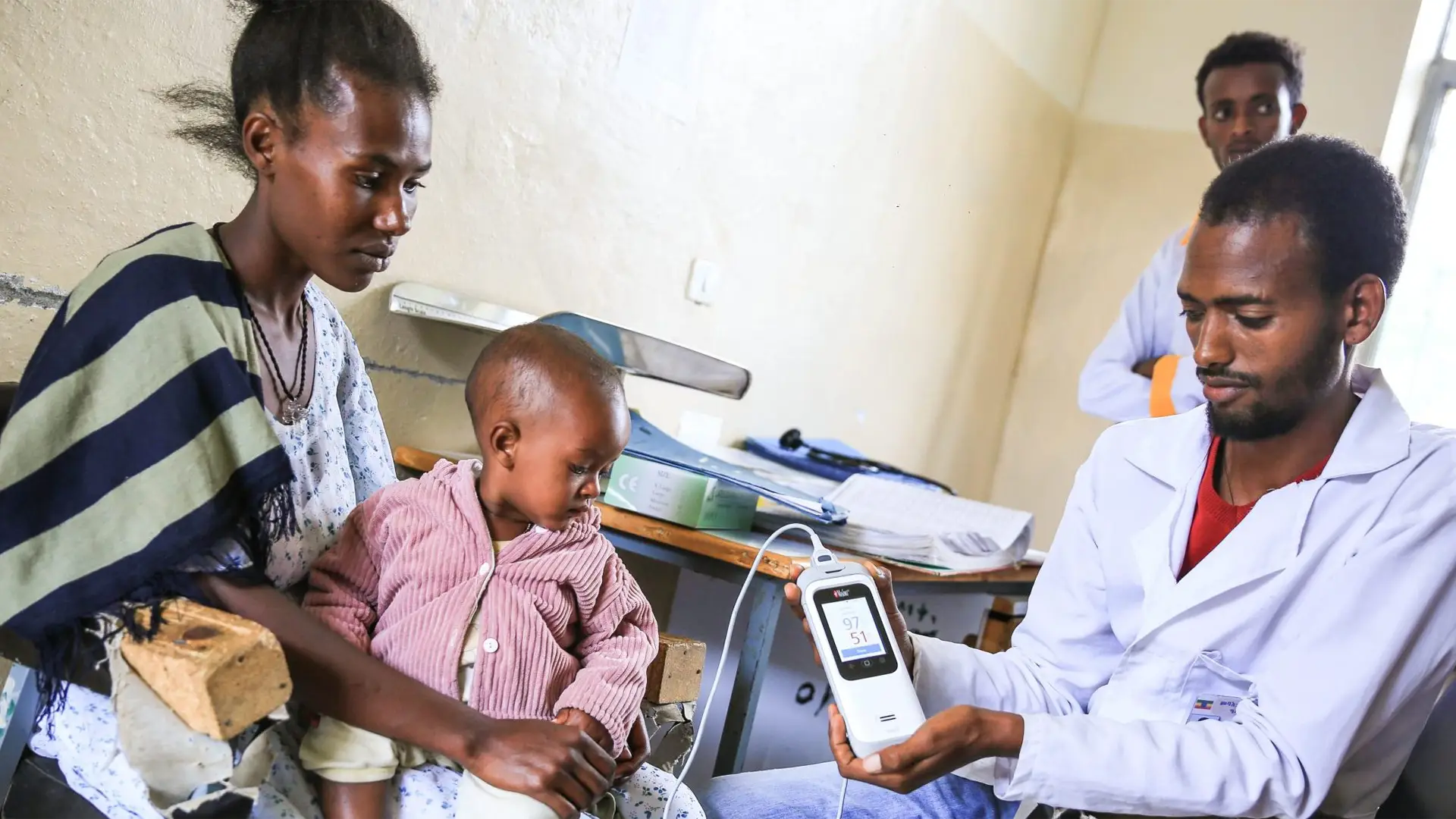 Photo of an Ethiopian nurse tending to a small child sitting on his mother's knee