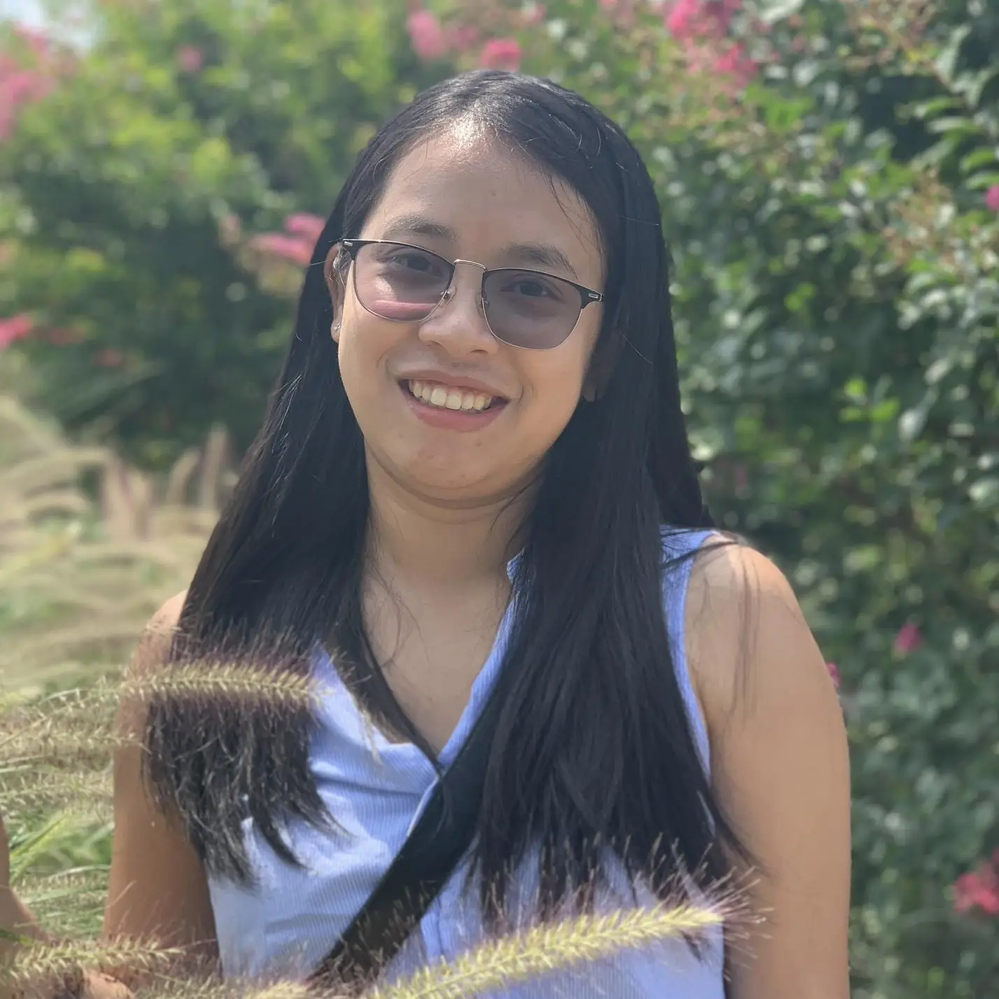 Headshot of a young Burmese woman with long black hair and sunglasses. She's in a garden