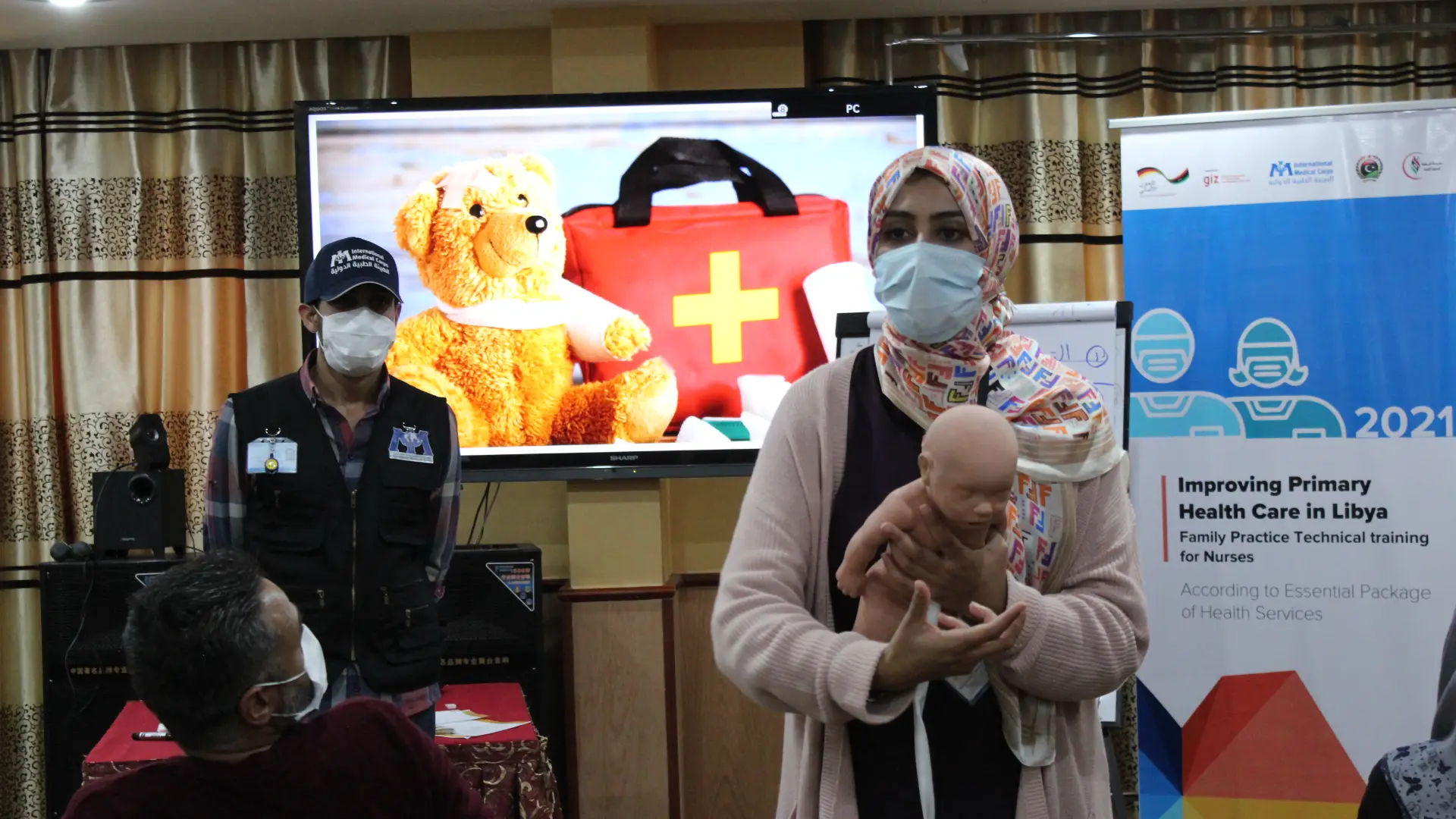 A masked Libyan woman demonstrates how to care for a baby (using a model) and the words 'Health systems strengthening in fragile states: picturing the views of international NGOs'