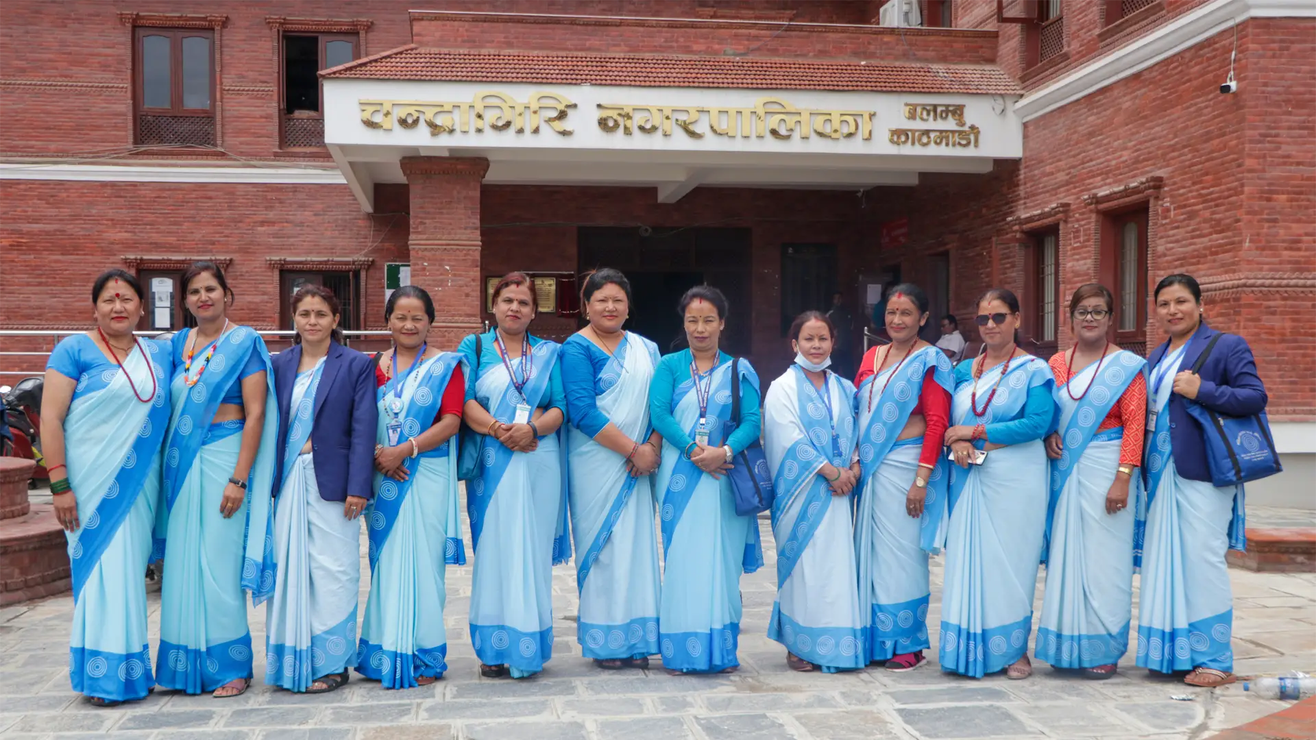 A row of 12 standing, smiling Nepali female community health volunteers - all are in blue saris