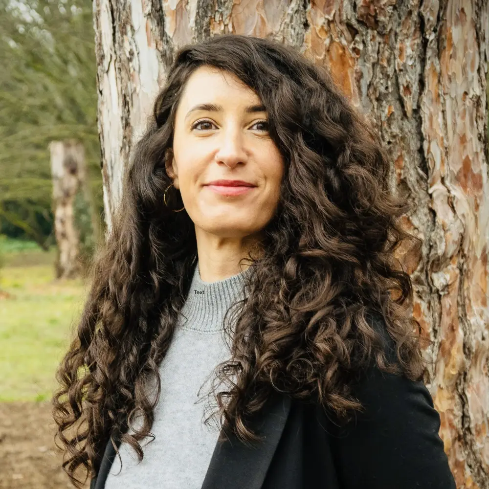 A headshot of a smiling European woman with long dark curly hair