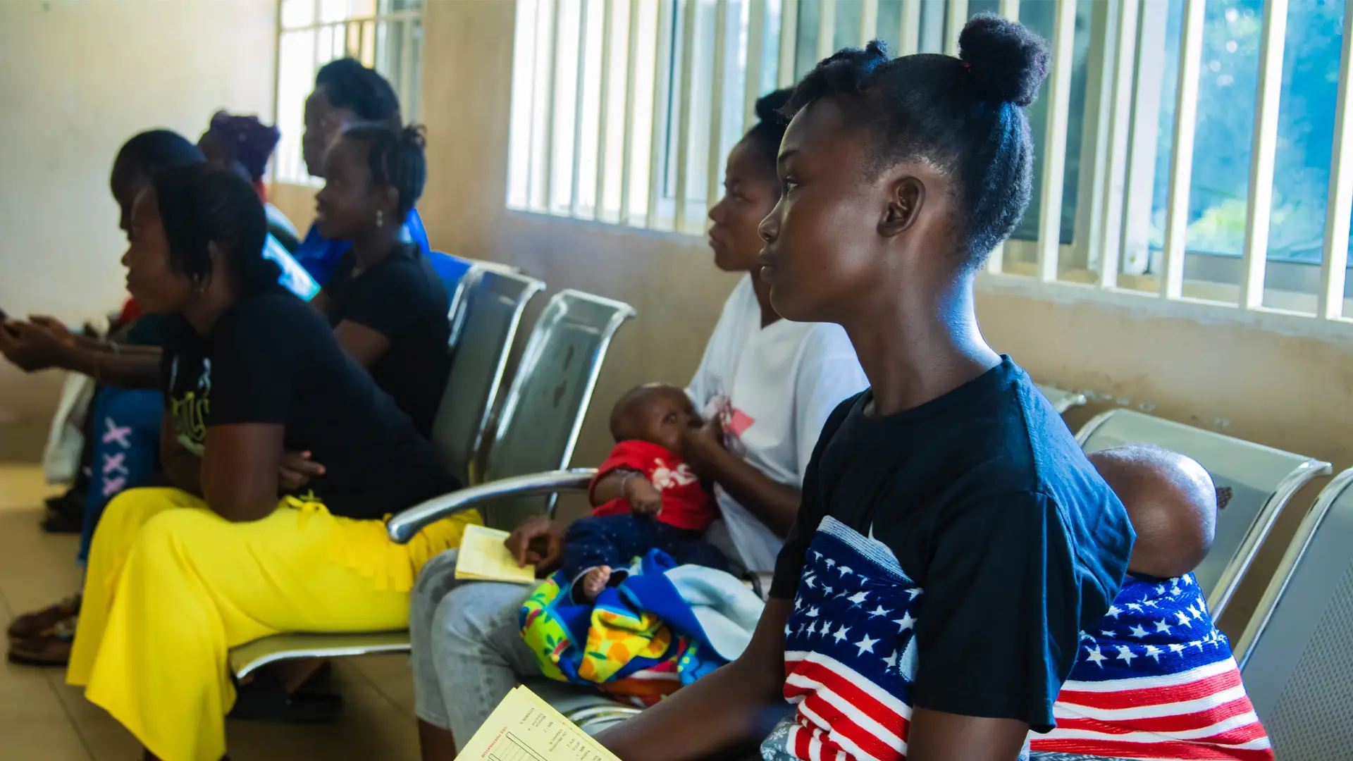 Young Sierra Leone women sit with babies in a waiting room