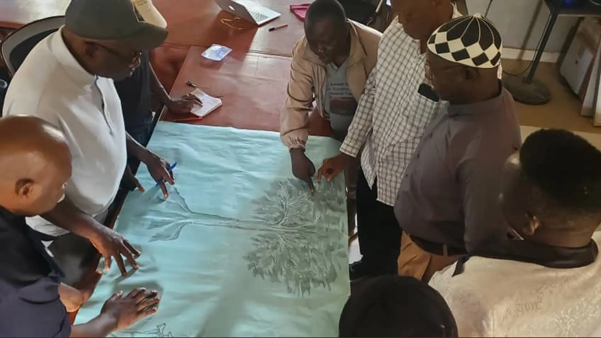 Seven Sierra Leonian men standing around a sheet of paper featuring a drawing of tree