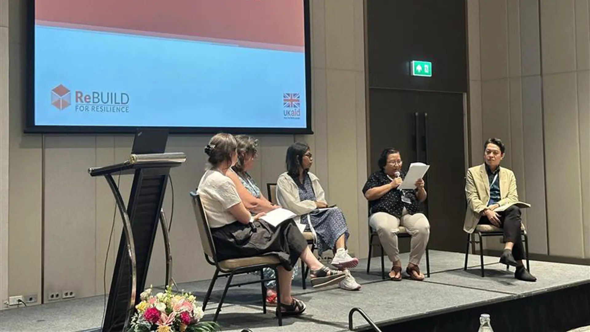 A photo of a stage in front of a big screen with 'ReBUILD' on and four women and a man speaking