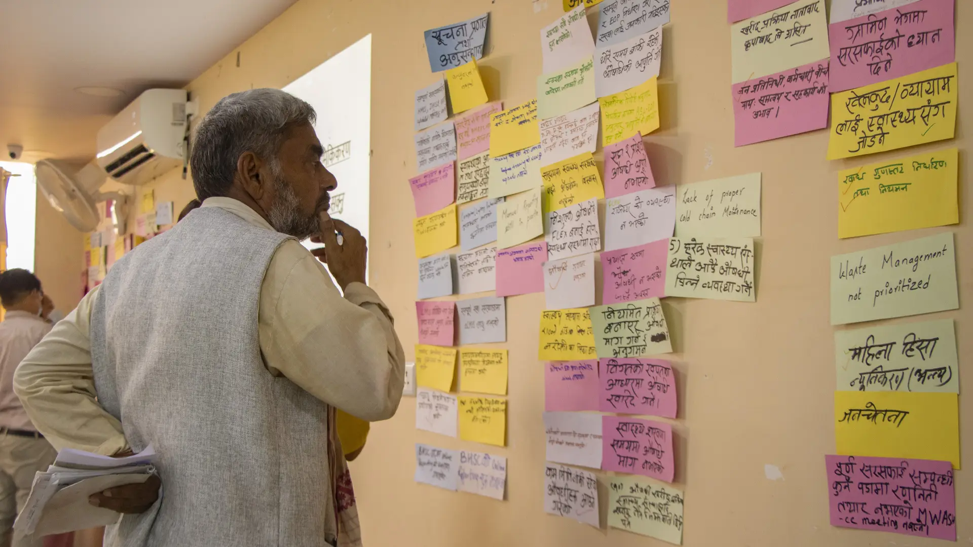Photo showing a Nepali man pondering a wall where lots of post-its have been placed. One says 'waste management not prioritised'