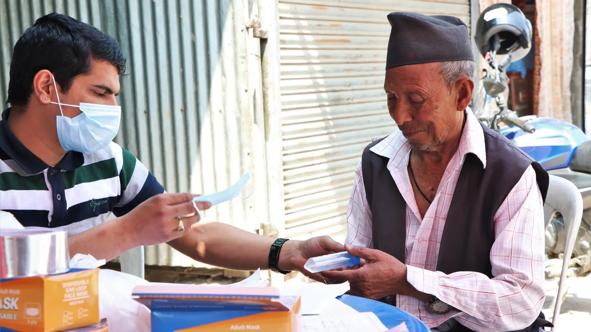Masked Nepali young man hands a COVID test to an older man