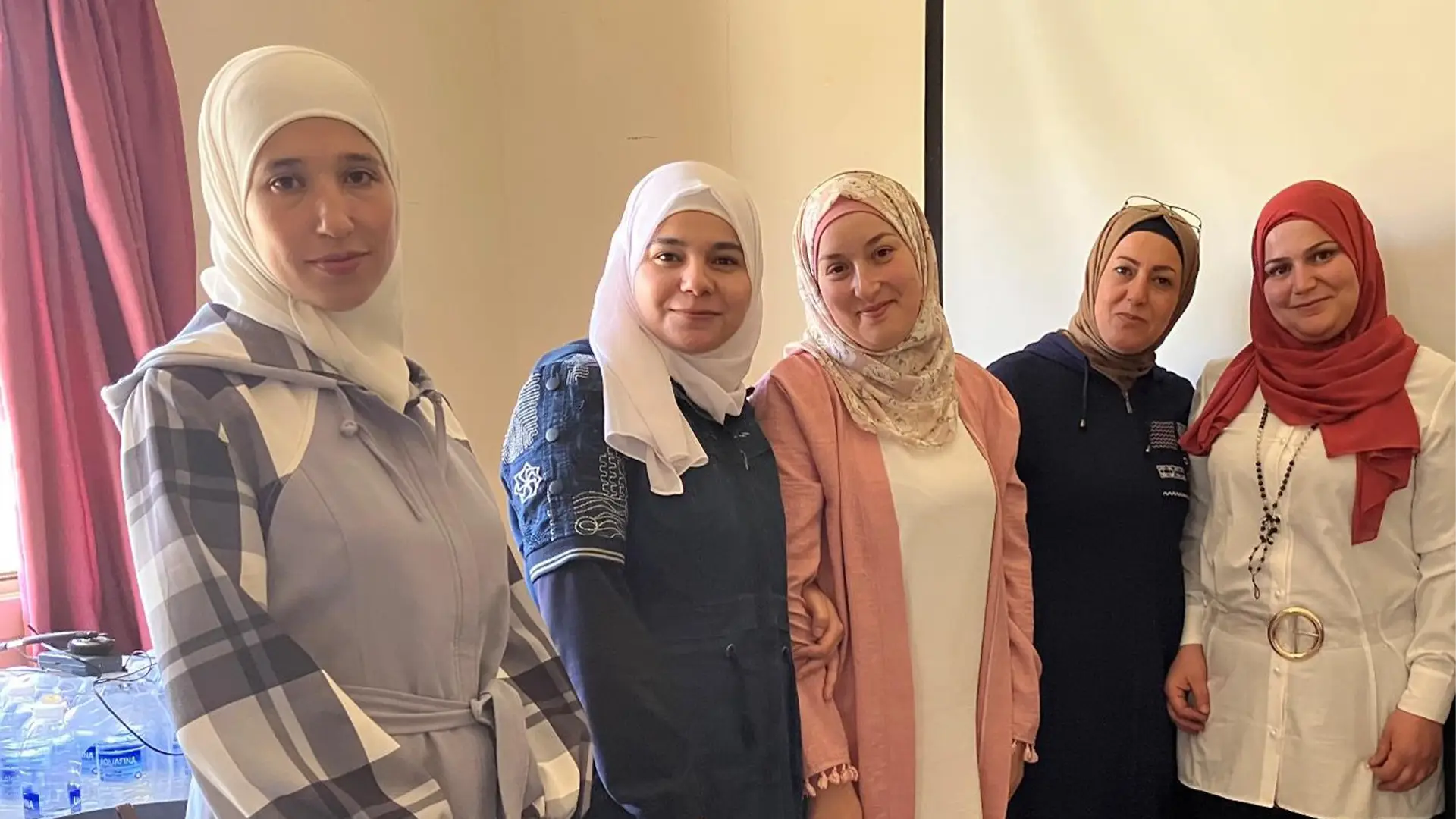 Five Syrian women stand in a line, smiling at the viewer
